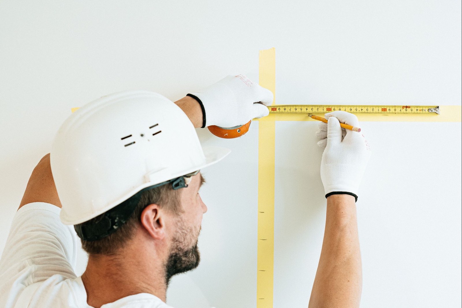 A builder in a hard hat measuring a wall with a tape