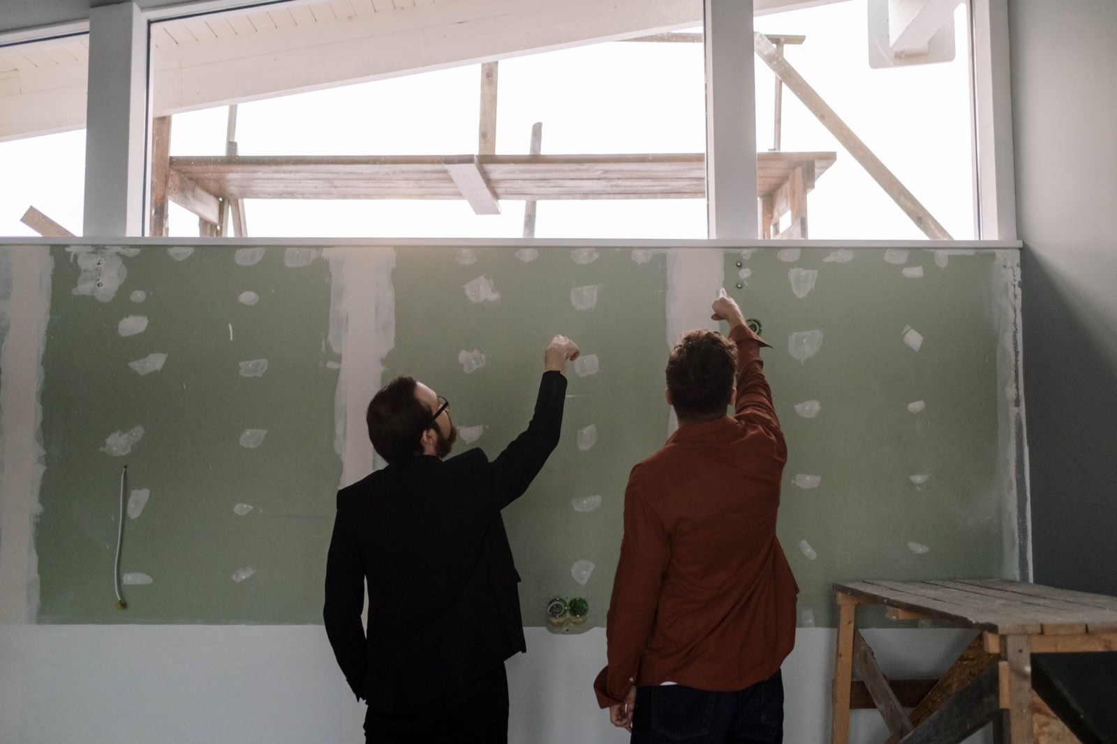 Two people pointing at a drywalled wall during a renovation