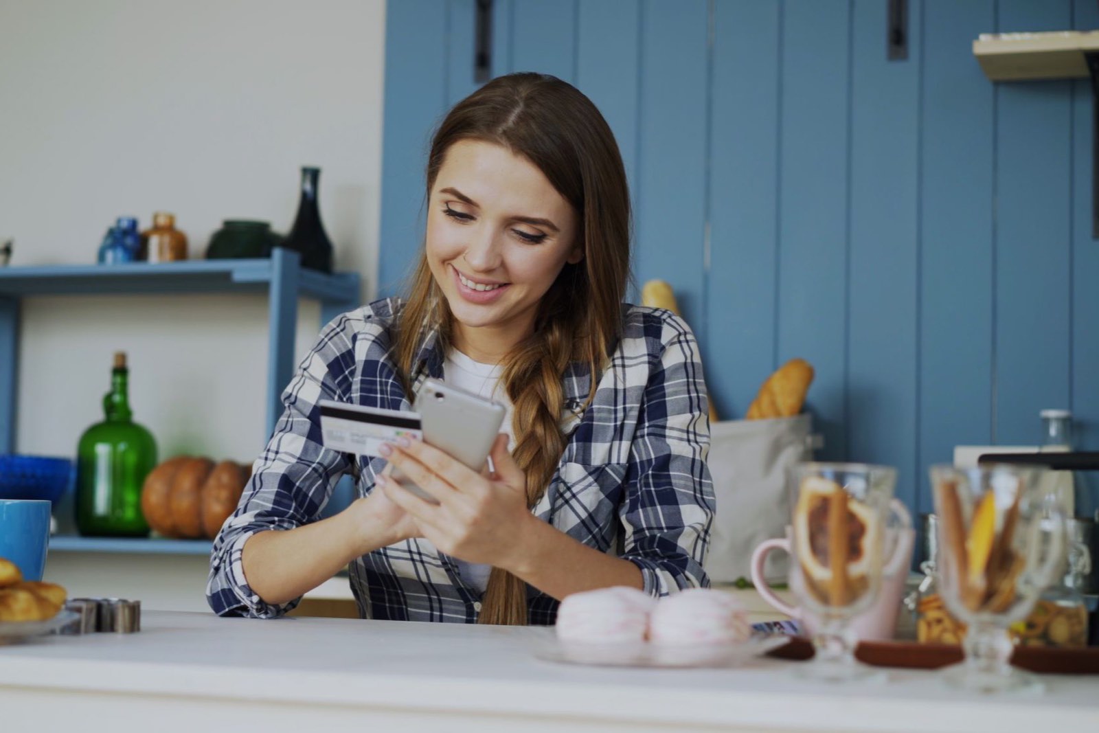 A homeowner paying on her phone with a card in hand at the kitchen counter