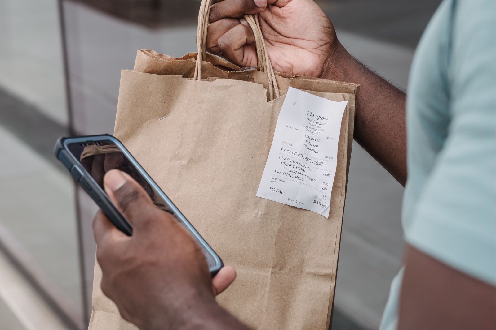 A hand holding a phone beside a paper bag with the receipt stapled to it