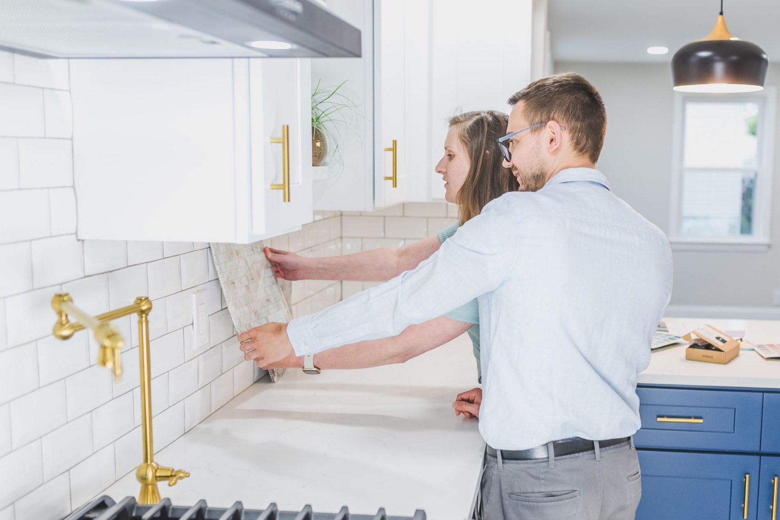 Two people holding up tile samples against a kitchen wall