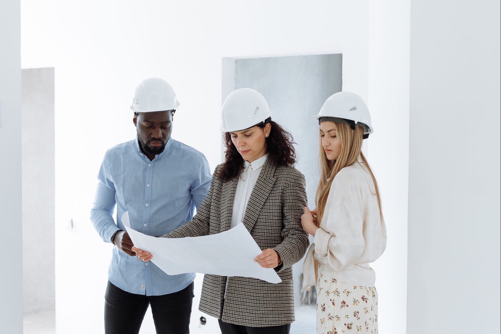 Three people in hard hats going over plans in a new room