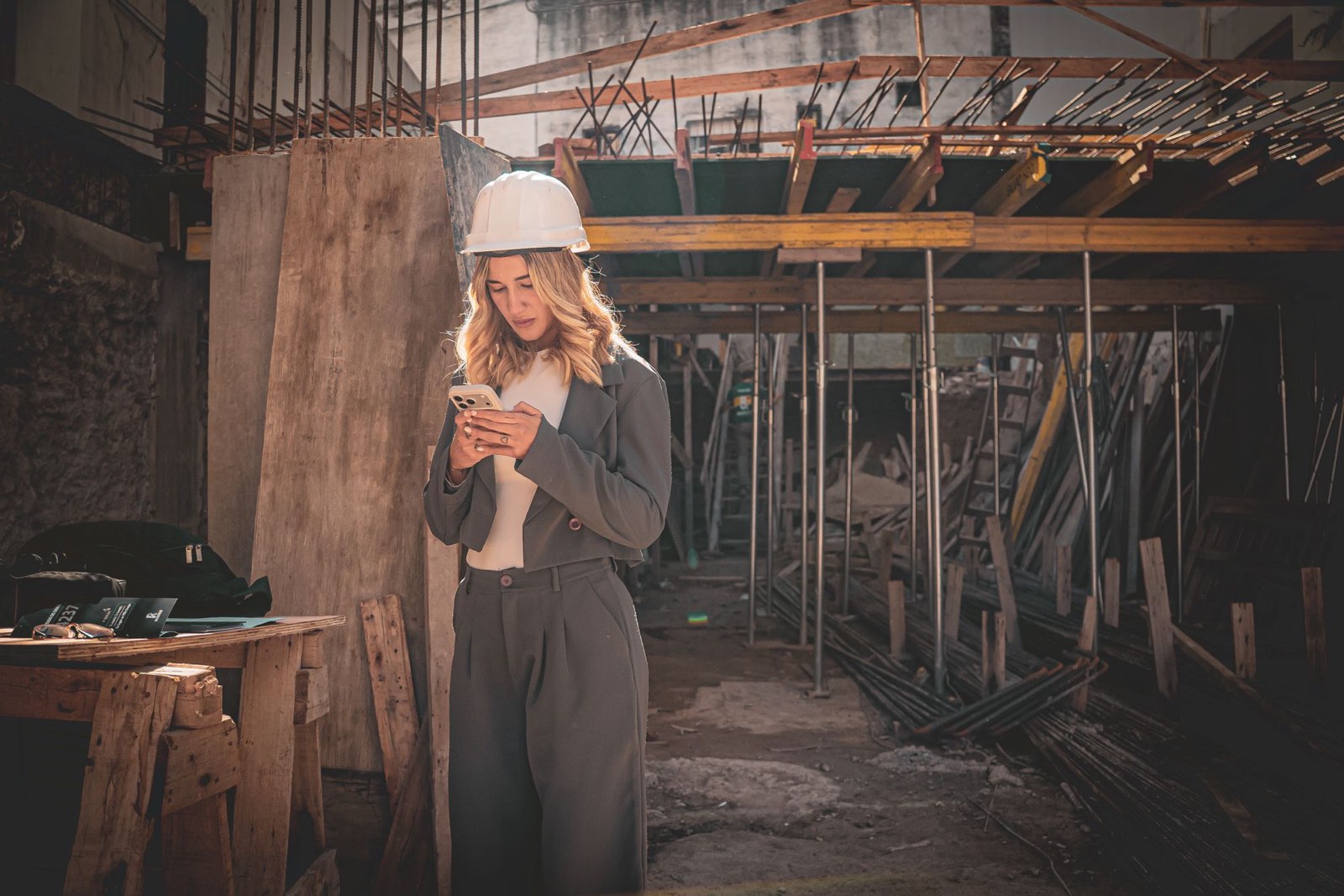 A worker in a hard hat checking her phone inside a building under renovation